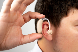 A person is holding a hearing aid near their ear, demonstrating its placement.