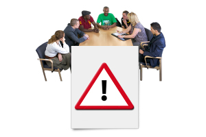 people sitting around a table with a poster of a hazard symbol - a red triangle with a black exclamation in the middle